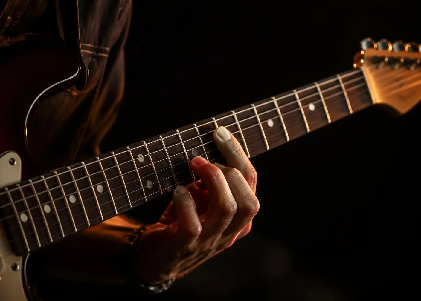 Mão de guitarrista sobre o braço de uma guitarra elétrica em luz âmbar